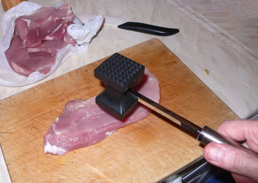 Photo of a meat tenderizer in use with a pork steak