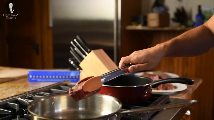 Placing A Steak In A Pan With Kitchen Tongs Photo of placing a steak in a pan with kitchen tongs