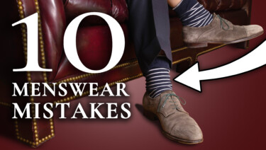 Raphael sits on a leather sofa in a navy suit and brown shoes; a large arrow points to his socks, which are sloppily sliding down his calves. Text reads, "10 Menswear Mistakes"