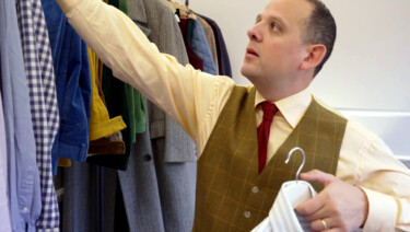 Raphael, in a yellow shirt, red tie, and brown vest, searches through the shirts he packed for Pitti Uomo 105
