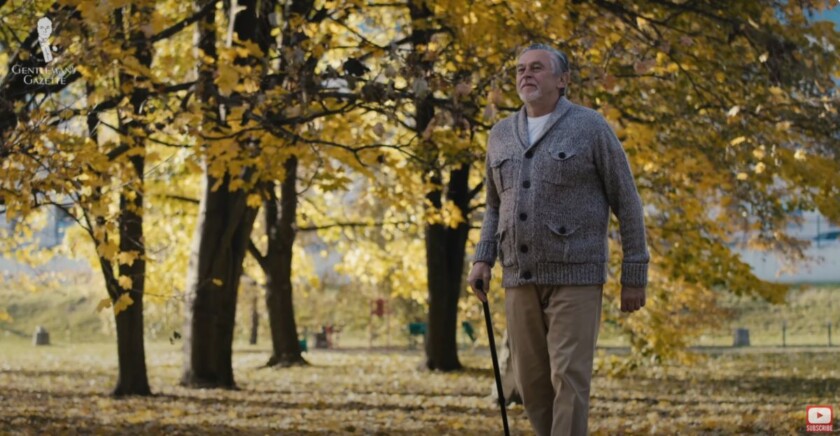 An old man walking outside with a cane