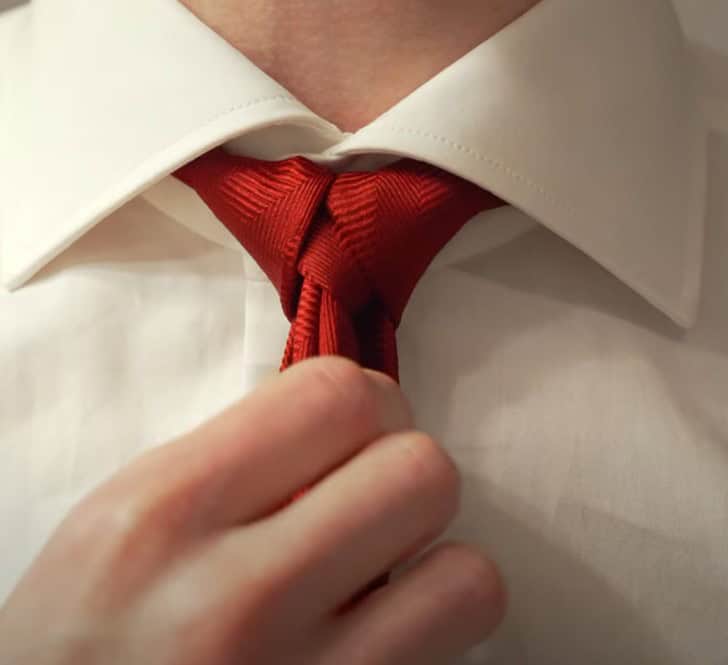 a person wearing an a red tie with a cape knot over a white dress shirt with a spread collar