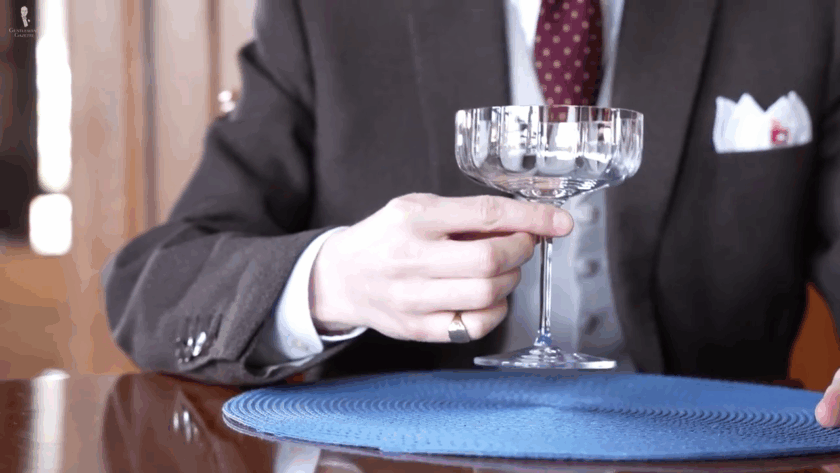 a hand gripping the upper stem of a coupe glass for stability