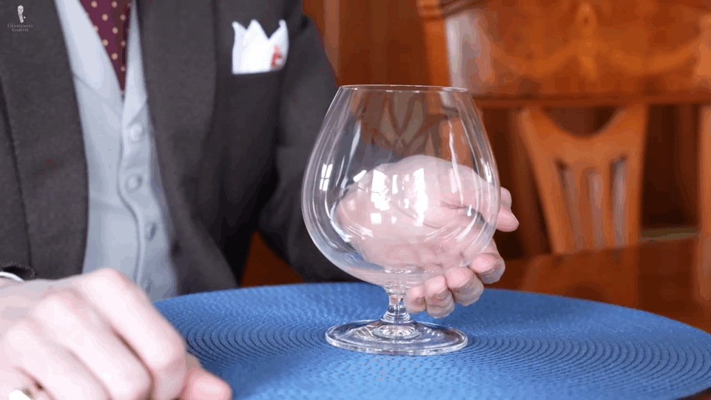 Hand holding a snifter glass by cupping the lower bowl, with the stem resting to one side