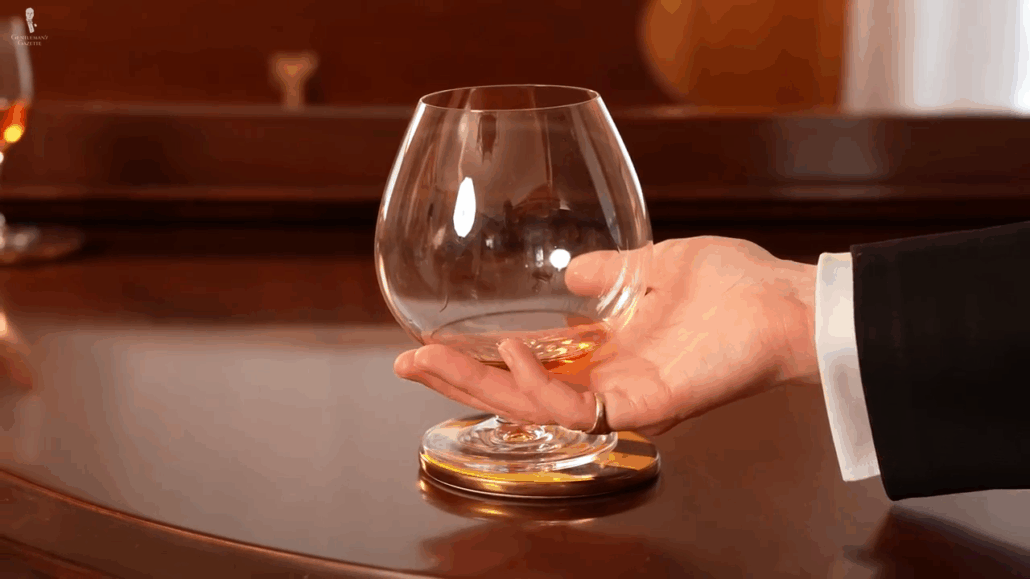 Hand grasping a snifter glass with fingers around the lower bowl and the stem aligned to the side