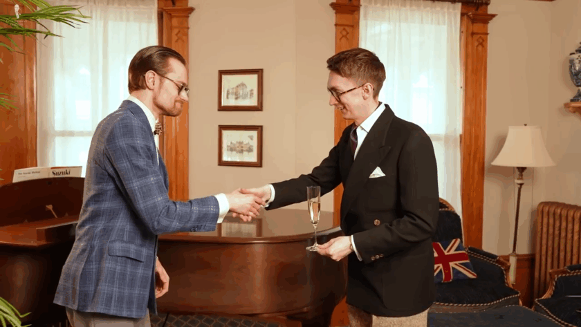 Jack briefly grips the foot of a Champagne flute so the stem is free as he reaches to shake Preston's hand 