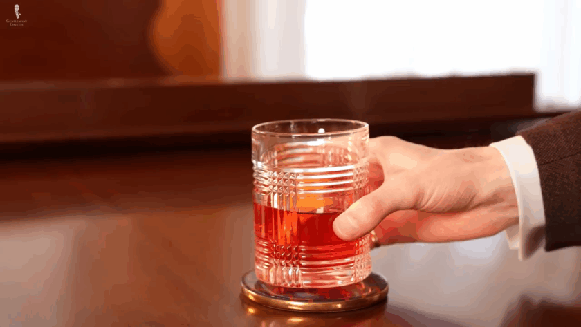 Man holding a lowball glass correctly by gripping higher up above the liquid level to prevent warming the drink.