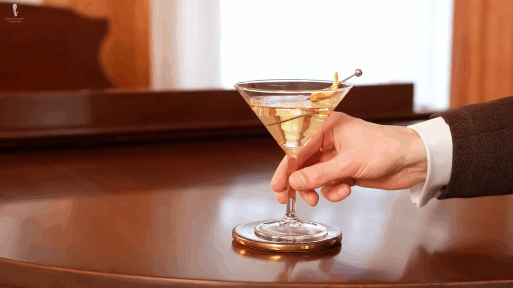 Hand holding a martini glass by the thicker stem using thumb, forefinger, and middle finger.