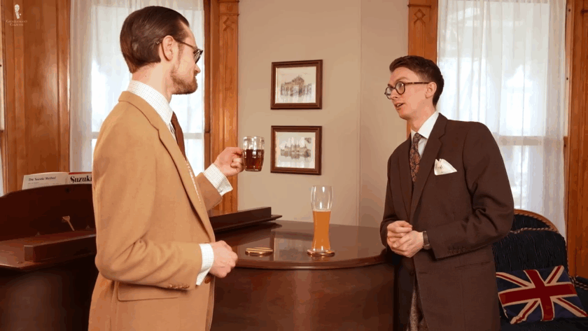 Two men enjoying drinks at a pub with a pint glass resting on the bar between them.