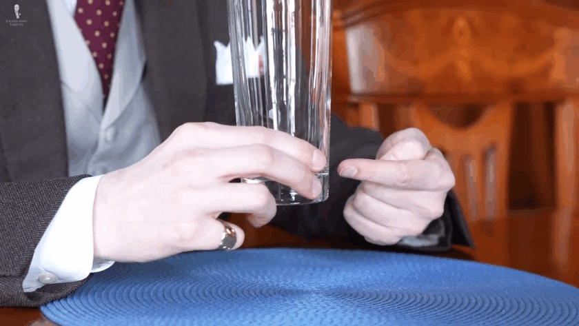 Man holding a tall highball glass delicately with two fingers near the base