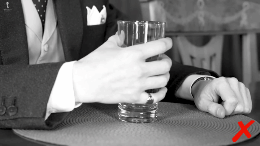 Man holding a tall highball glass with the whole hand wrapped around it