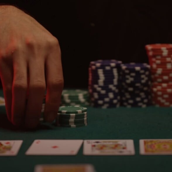 Gentleman Vice Gambling Wager For Fun a hand placing green poker chips on a card table, with stacks of blue, red, and white chips in the background and playing cards laid out