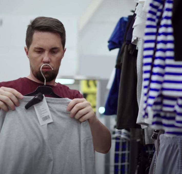 fast fashion promotes frequent replacement Man in a clothing store examining a gray t-shirt, representing the low-quality, trend-driven nature of fast fashion.