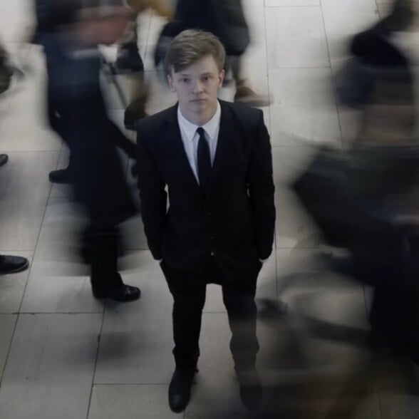 resentment toward formal dress history Young man in a suit standing still among a blurred crowd