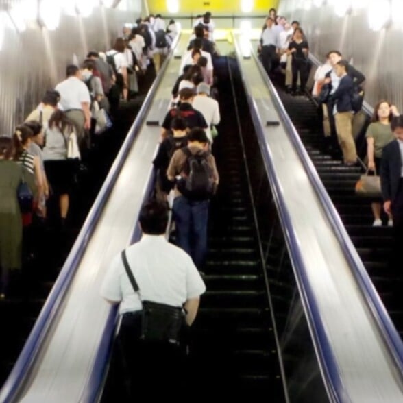 Commuter standing on the left side of a long escalator in Japan.