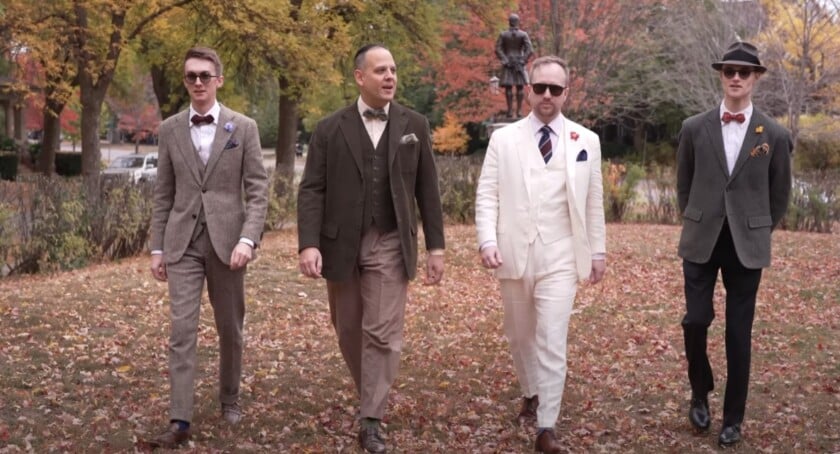 Four men in tailored suits walking together in autumn park
