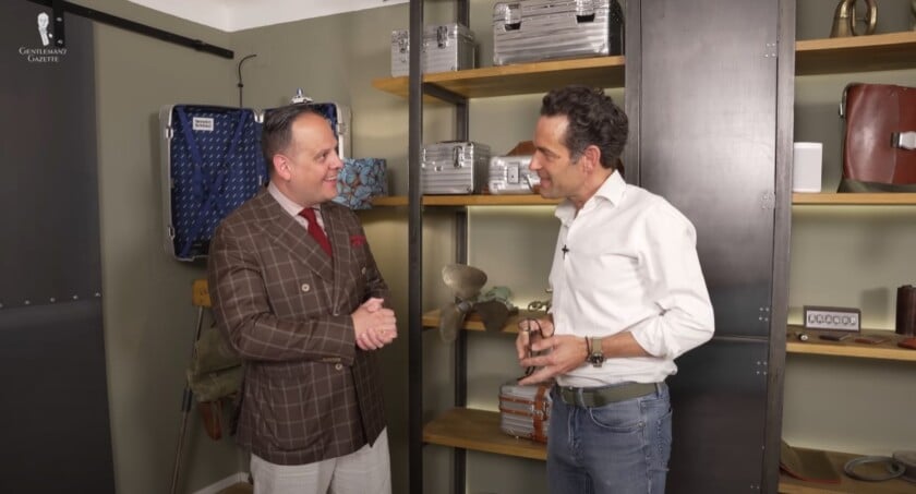 raphael outfit unicum wien atelier tour vienna Sven Raphael Schneider in a brown windowpane suit jacket in conversation with Bernd Schreiner, founder of Unicum Wien , inside his Viennese showroom filled with custom aluminum suitcases.