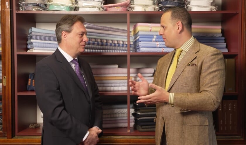 Sven Raphael Schneider wearing a tobacco brown linen sport coat and yellow knit tie talking to Master Tailor Robert Ruzicka inside the historic Zum Jockey Club shop in Vienna.