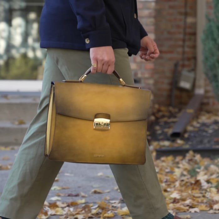 vintage st dupont briefcase yellow patina brass lock A vintage S.T. Dupont leather briefcase with a unique yellowish patina and gold-plated brass lock being carried by a man in green trousers.
