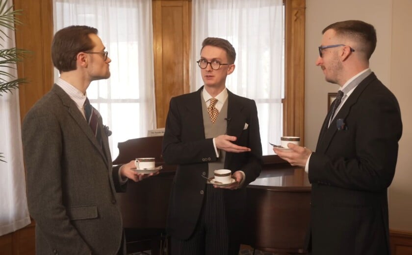 Three men standing and holding teacups with saucers during a formal tea gathering.