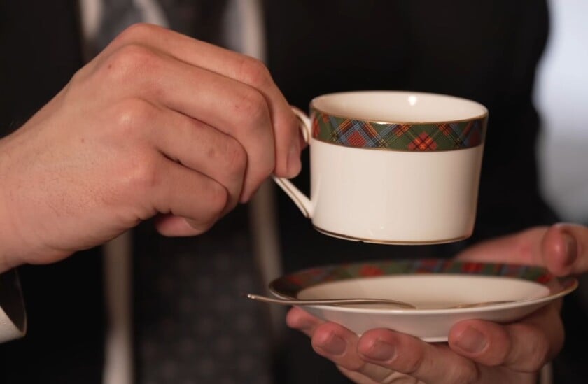 Hand holding a teacup by pinching the handle between the thumb and forefinger during tea service.