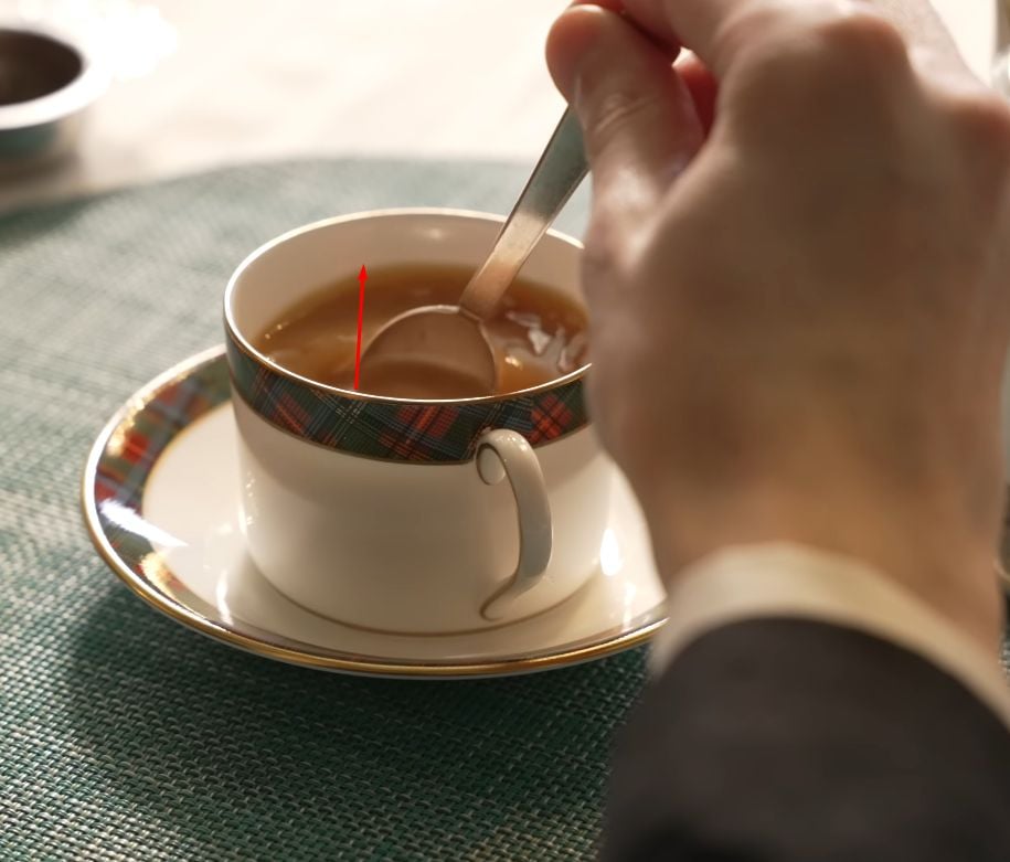 Hand stirring tea in a teacup with a teaspoon using a back-and-forth motion instead of swirling.
