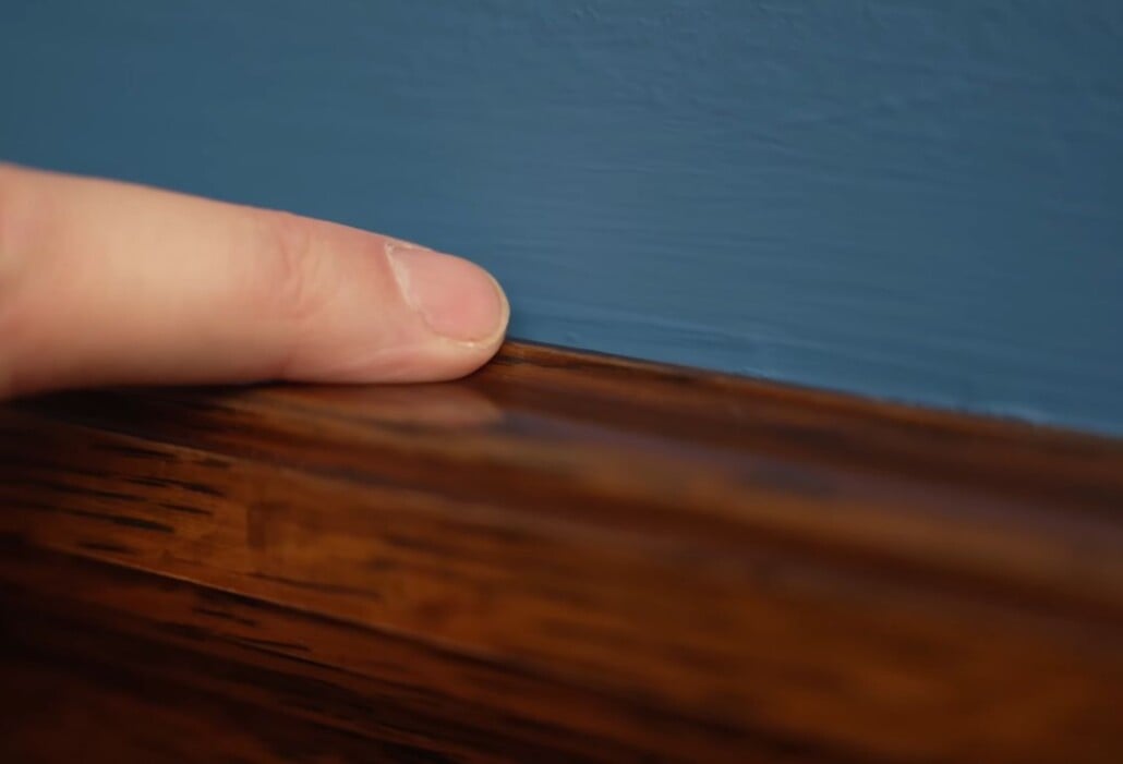 Close-up of a finger highlighting the dark crevice between a wooden baseboard and a wall where clothes moths frequently breed.