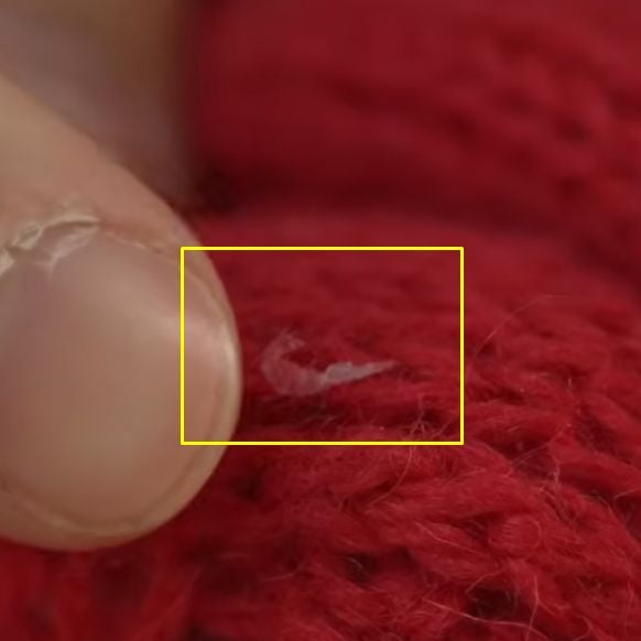 Macro shot of translucent white silken webbing and cocoon residue left by clothes moth larvae on a red knit wool fabric, highlighted by a yellow box.