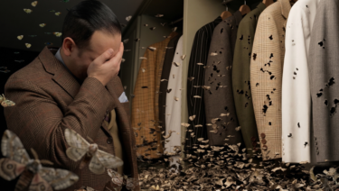 Man in a brown checked jacket covering his face beside a closet full of moth-damaged jackets, surrounded by swarming clothes moths.