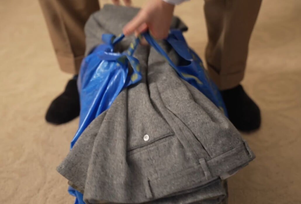 Close-up of a person packing grey wool trousers into a large blue IKEA bag for transport to a freezer for moth larvae treatment