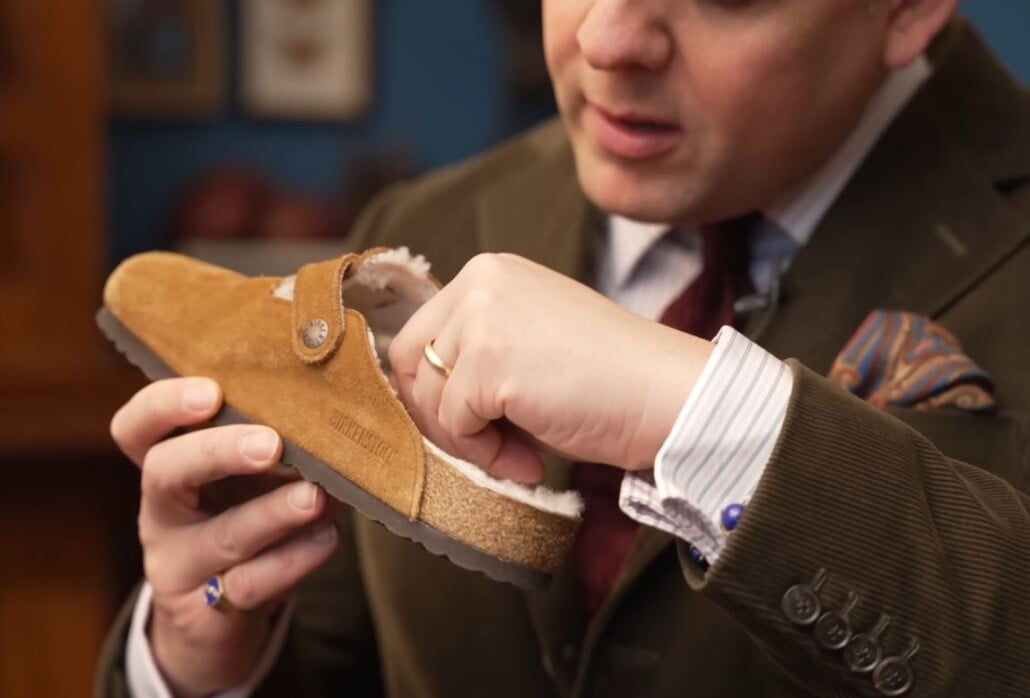 A man examining the interior shearling lining of a suede clog for signs of a clothes moth infestation.