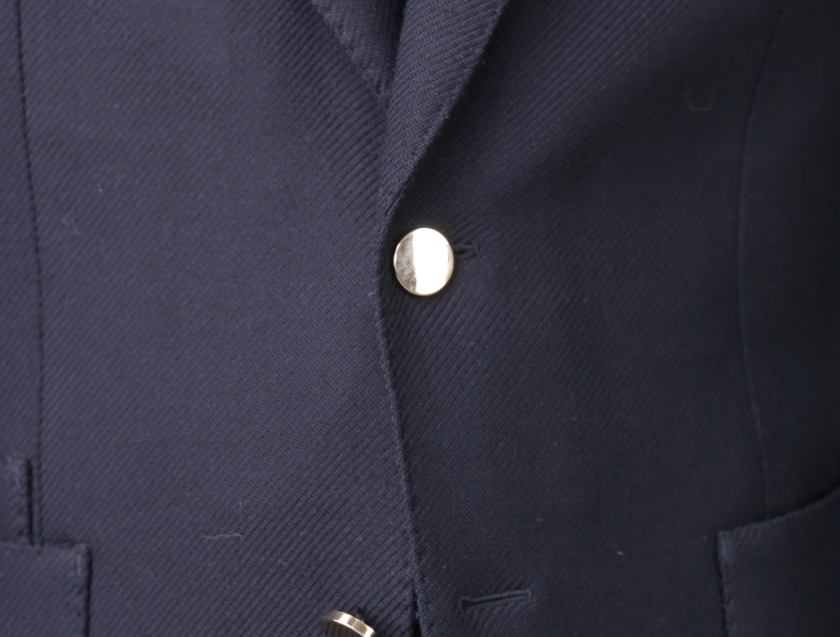 Close-up of a navy blue textured jacket featuring a polished gold button.