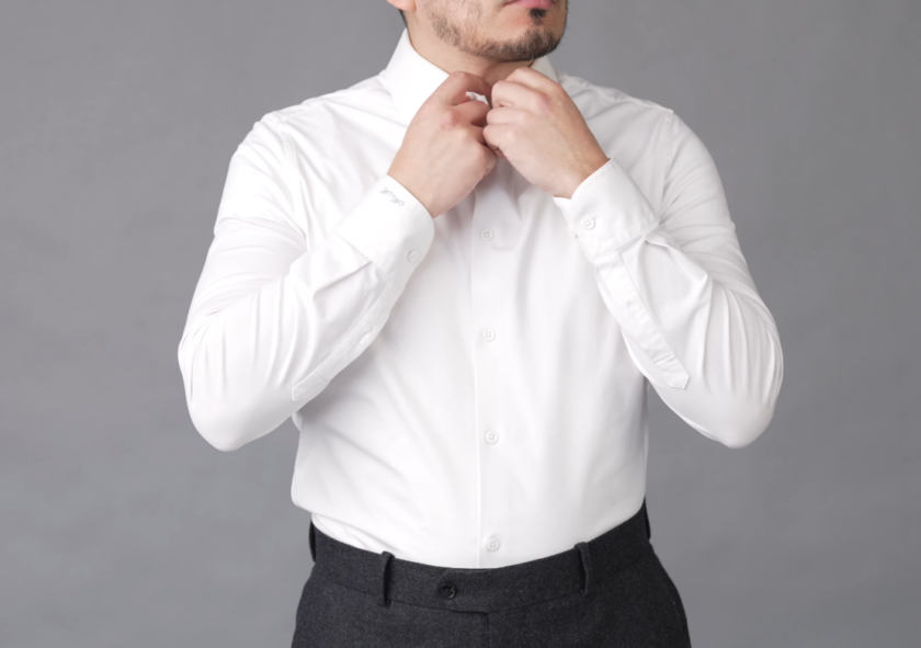 Ivan adjusting the collar of a crisp white dress shirt paired with dark trousers.
