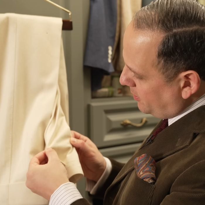 Raphael meticulously inspects the folded cuffs of off-white wool trousers in a closet to check for signs of moth eggs or larval activity.