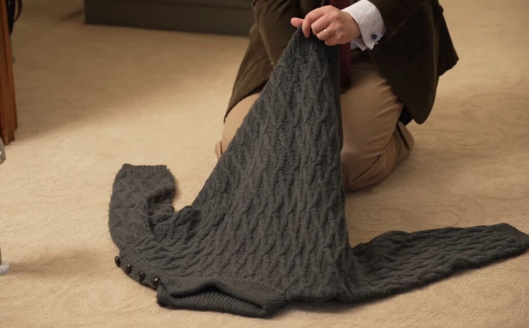 A man kneeling on a carpeted floor, spraying vodka inside a knitwear