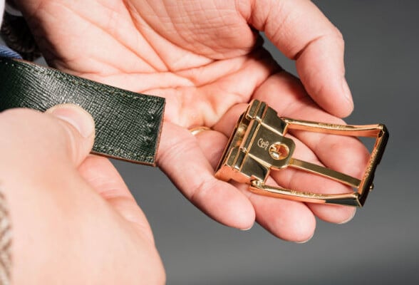 A hand holds a gold belt buckle