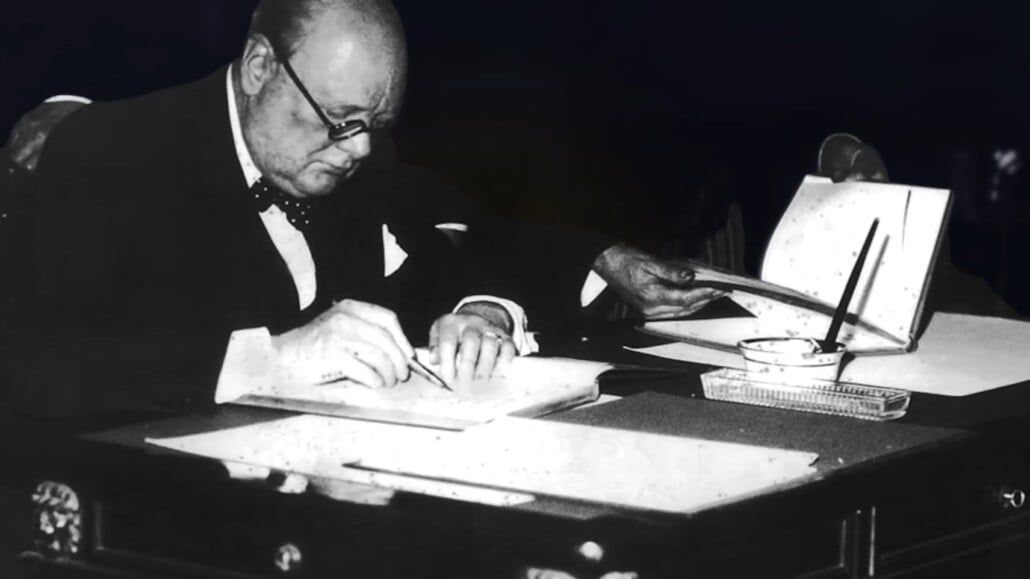 Photograph of Winston Churchill at a desk writing with a fountain pen.
