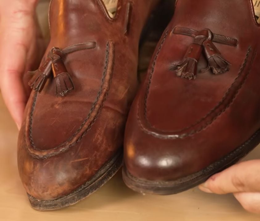 A close-up of a pair of brown leather tassel loafers held by a person's hands, displaying a before-and-after restoration comparison. The shoe on the left is dull, scuffed, and faded, while the shoe on the right is freshly polished, shiny, and restored to a rich, dark brown color.