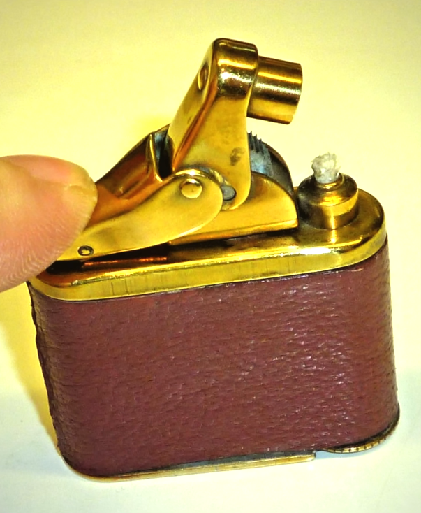 Lighter A close-up of a thumb pressing the mechanical lever of a vintage pocket lighter, which features a gold-toned top ignition mechanism and a burgundy leather-wrapped body