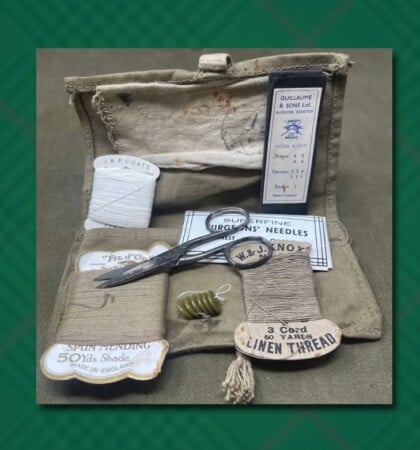 Vintage Housewife Compact Sewing Kit An open vintage canvas sewing kit, known as a housewife, displaying small metal scissors, green buttons, a packet of needles, and various spools of mending and linen thread.