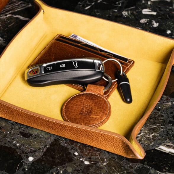 Round Saddle Brown Dumont Leather Key Fob Fort Belvedere R5 0267 4000X4000 1 A brown leather key fob attached to a car fob next to a leather card holder in a leather valet tray.