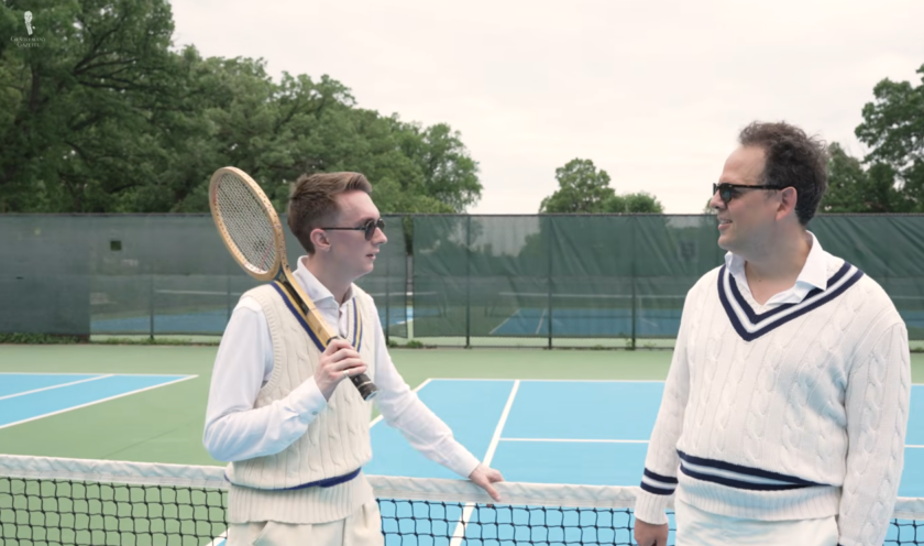 GG Tennis White Sweater Court Test Two men wearing cable-knit tennis sweaters and vintage tennis whites stand at a net on an outdoor court