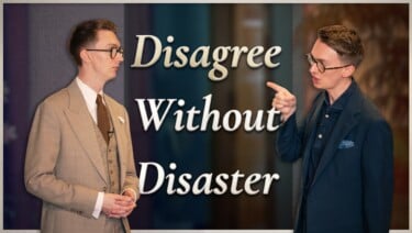 Two men facing each other in mid-disagreement, one in a tan three-piece suit listening calmly while the other in a navy jacket points and speaks. Text reads: "Disagree Without Disaster"