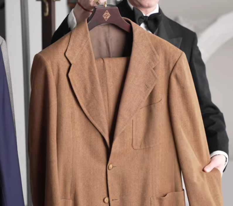 Ginger Herringbone Two Piece Suit Patch Pockets Ginger-toned herringbone two-piece suit jacket with notch lapels and patch pockets, held up on a wooden hanger