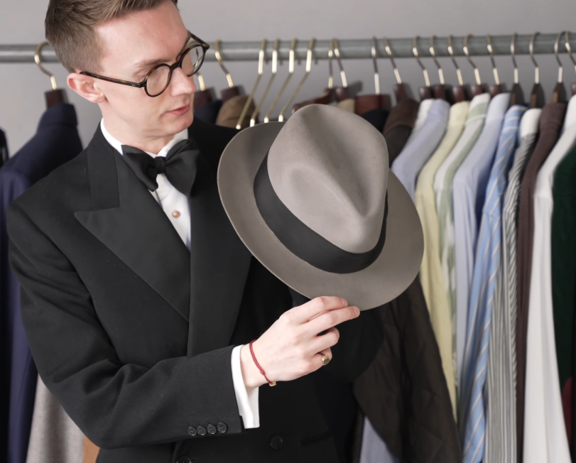 Gray Felt Center Crease Snap Brim Hat Jack Collins holding a gray felt center-crease snap brim hat with a dark grosgrain band, in front of a rail of shirts and jackets