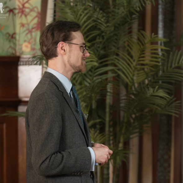 man unbothered flat response tweed jacket A man in a gray-green tweed jacket and dark tie standing in profile with a neutral, unbothered expression