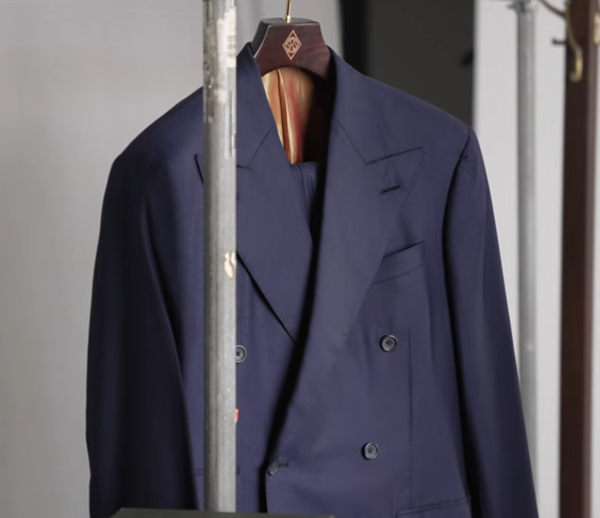 Navy Double Breasted Suit Jacket Peak Lapel Navy double-breasted suit jacket with peak lapels hanging on a clothing rail
