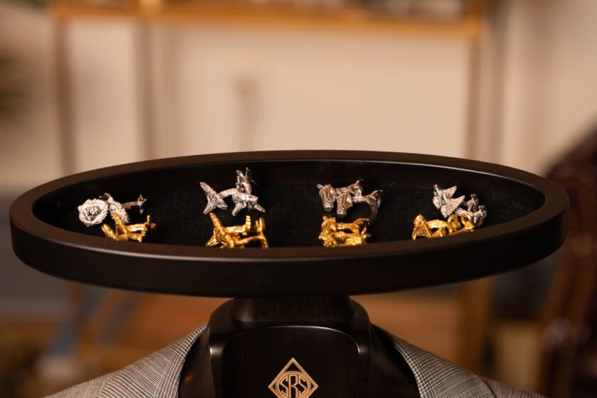 Several pairs of animal-shaped cufflinks in silver and gold arranged on a dark wooden valet tray with a black felt lining