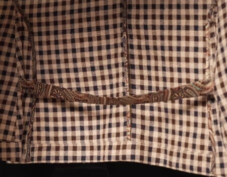 Close-up of a checked sport coat's back vent, with a patterned fabric strap bridging the two vent edges