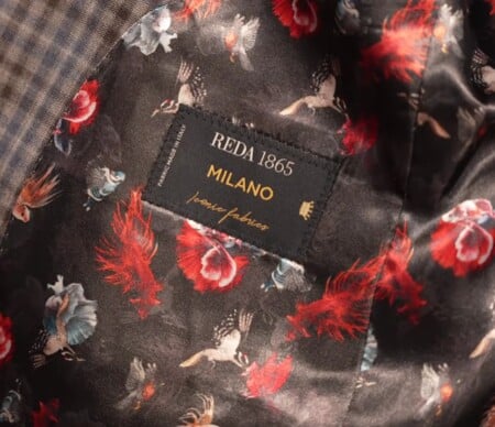 Bold black jacket lining patterned with red flowers, feathers, and game birds, with a sewn-in Reda label. Text reads: "REDA 1865 MILANO Iconic Fabrics. Fabric Made in Italy."